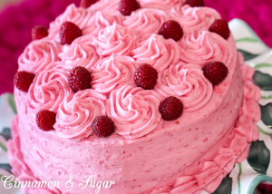 Raspberry cake is an almond scented white cake layered with raspberry buttercream and raspberry jam, with no artificial coloring. The perfect cake to celebrate any special occasion, especially Valentine's Day! Recipe shared with permission granted by Lucy Burdette, author of Fatal Reservations. 