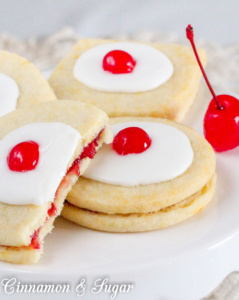 Empire Biscuits are flaky shortbread cookies that sandwich tart raspberry preserves and are then topped with sweet icing and colorful maraschino cherries. The perfect accompaniment to afternoon tea!