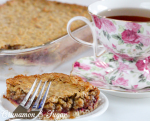 Crunchy brown sugar crust is layered with simple raspberries and topped with a gooey-chewy nut and coconut layer to make Raspberry Bars a satisfying treat! Recipe shared with permission granted by Ellie Alexander, author of cozy mystery LIVE AND LET PIE.