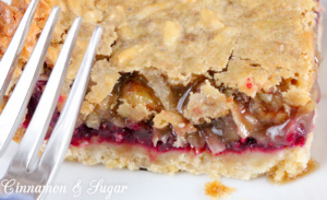Crunchy brown sugar crust is layered with simple raspberries and topped with a gooey-chewy nut and coconut layer to make Raspberry Bars a satisfying treat! Recipe shared with permission granted by Ellie Alexander, author of cozy mystery LIVE AND LET PIE.