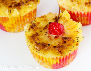 A rich, buttery pineapple cake topped with a caramelized pineapple ring and maraschino cherry make Pineapple Upside-Down Cupcakes perfect for hot summer months! Recipe shared with permission granted by Jenn McKinlay, author of DYING FOR DEVIL'S FOOD.