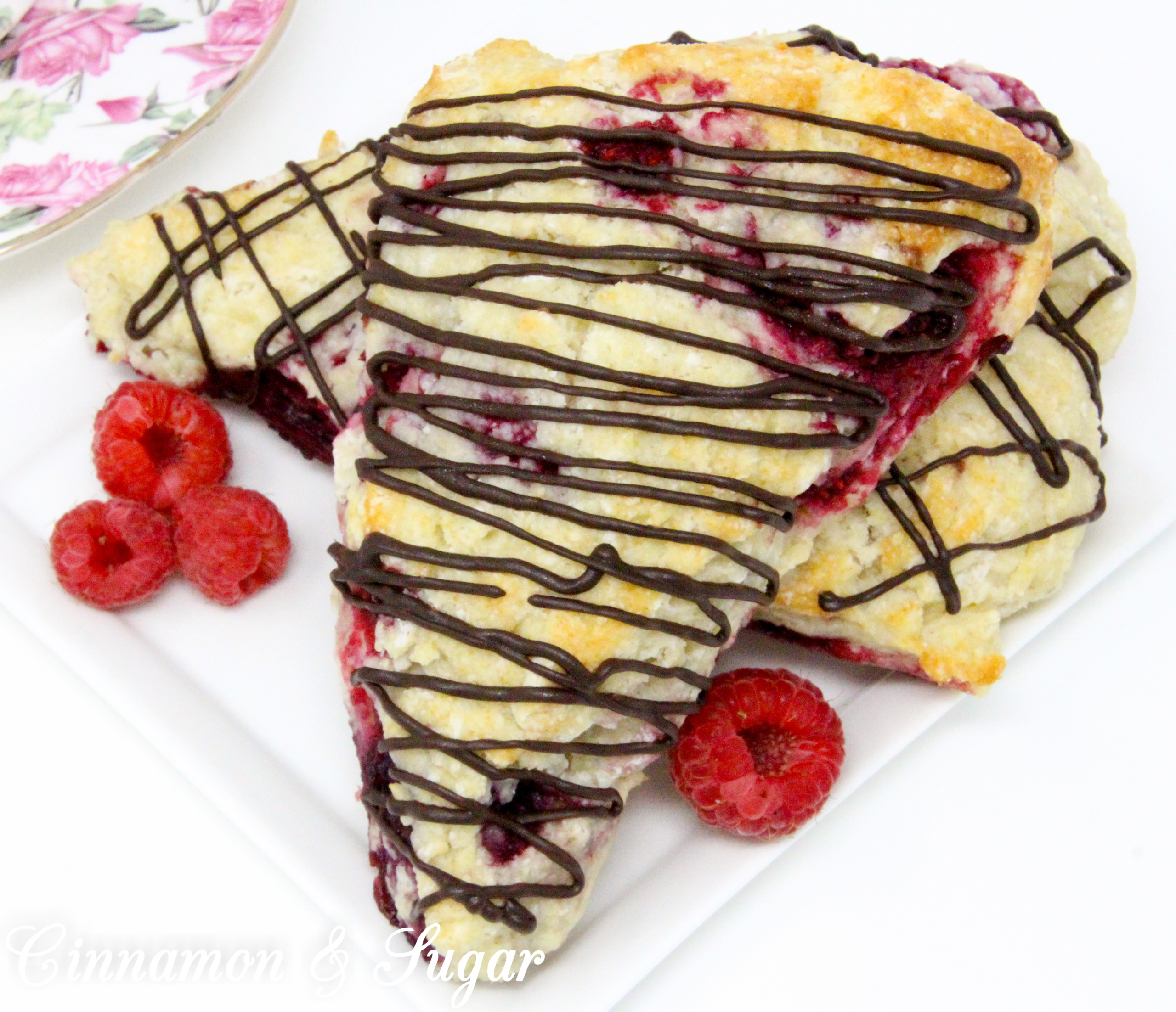 Raspberry Scones with Dark Chocolate Drizzle are rich, flaky, and flavorful, thanks to the addition of lemon oil and lemon peel, plus loads of raspberries. Drizzled with dark chocolate, the results are a scrumptious combination! 