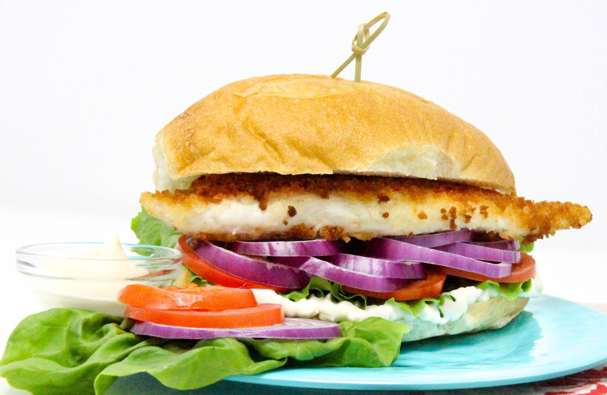 Fischbrötchen (German Fish Sandwich) uses a thin, pan-fried fillet, coated with breadcrumbs for a crispy exterior, and is layered with lettuce, red onions, peppers, and tomatoes for a delicious and hearty sandwich. Recipe shared with permission granted by T.C. LoTempio, author of MURDER FAUX PAWS.