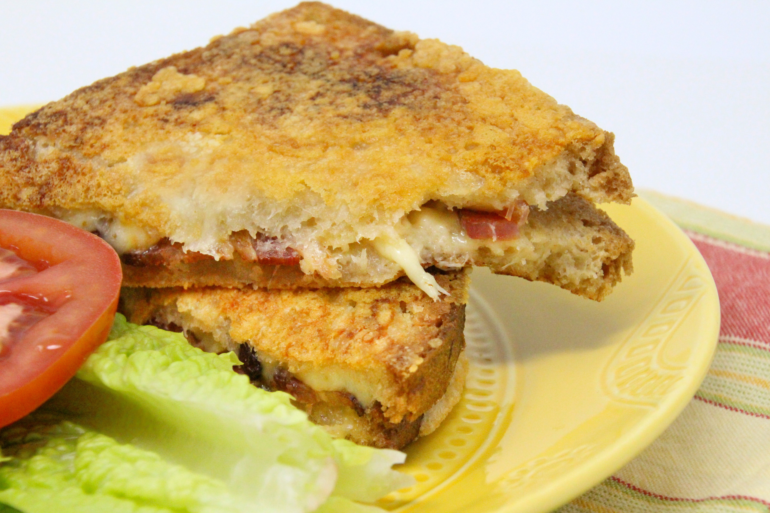 Smoky Steals the Bacon grilled cheese sandwich features bacon cradled by smoked gouda oozing between the slices of asiago bread. With the addition parmesan cheese sprinkled in the pan before grilling the bread, this sandwich is heavenly! Recipe shared with permission granted by Linda Reilly, author of UP TO NO GOUDA. 