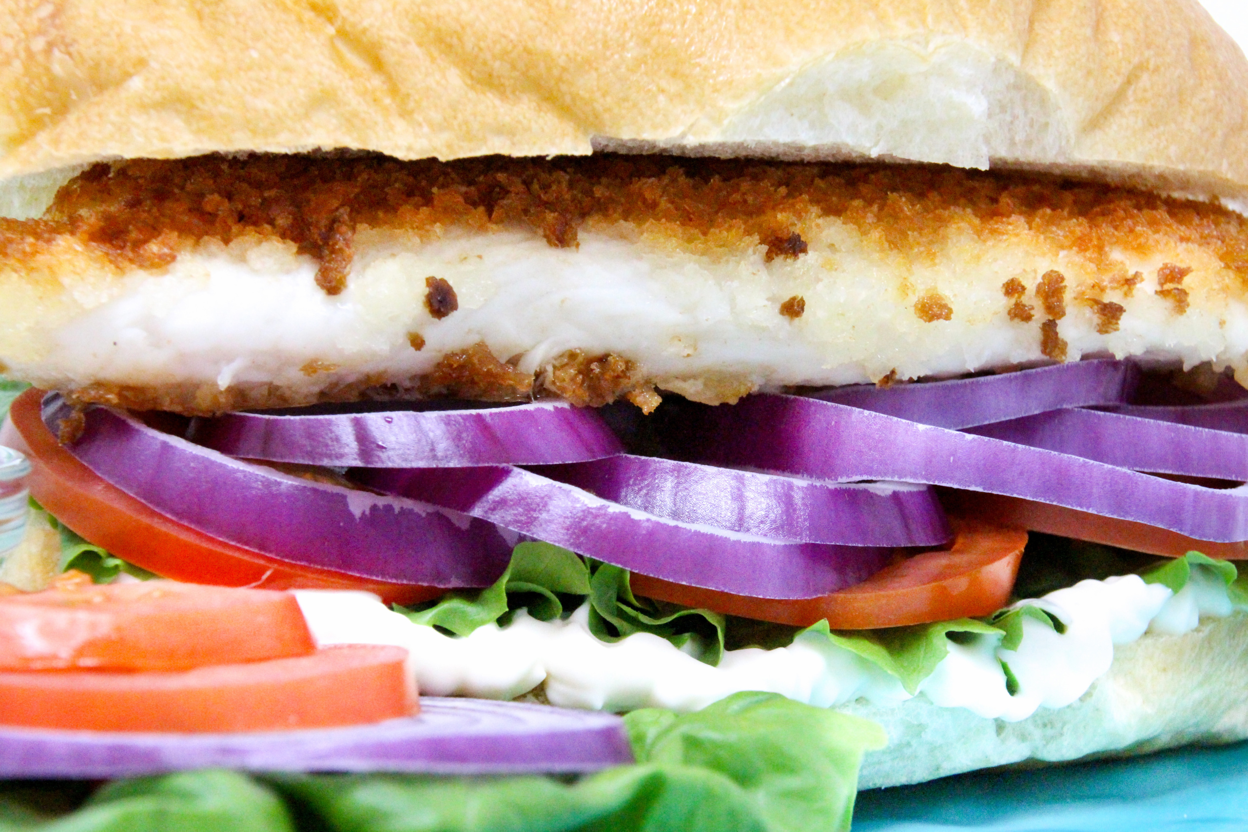 Fischbrötchen (German Fish Sandwich) uses a thin, pan-fried fillet, coated with breadcrumbs for a crispy exterior, and is layered with lettuce, red onions, peppers, and tomatoes for a delicious and hearty sandwich. Recipe shared with permission granted by T.C. LoTempio, author of MURDER FAUX PAWS.