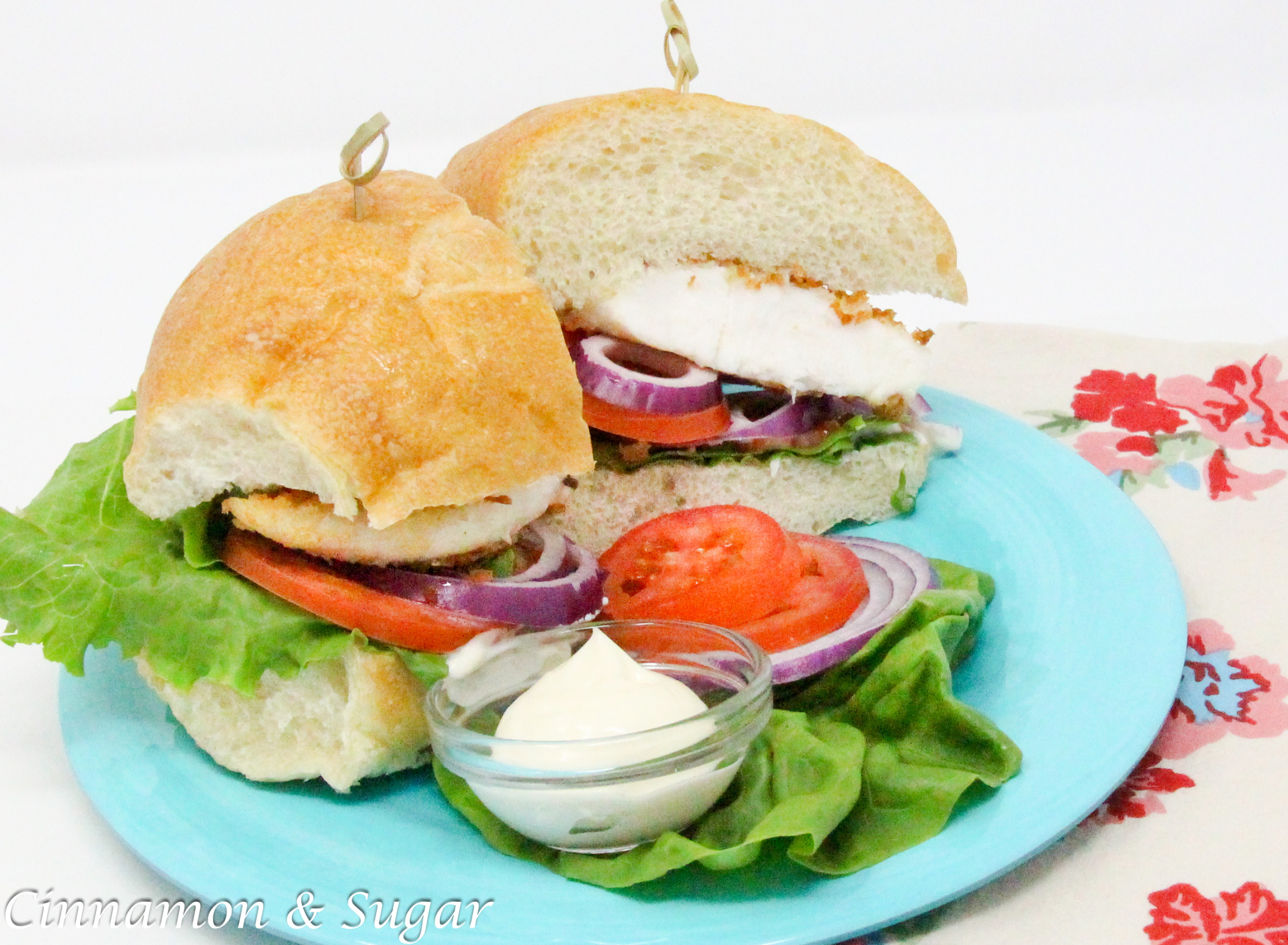 Fischbrötchen (German Fish Sandwich) uses a thin, pan-fried fillet, coated with breadcrumbs for a crispy exterior, and is layered with lettuce, red onions, peppers, and tomatoes for a delicious and hearty sandwich. Recipe shared with permission granted by T.C. LoTempio, author of MURDER FAUX PAWS.