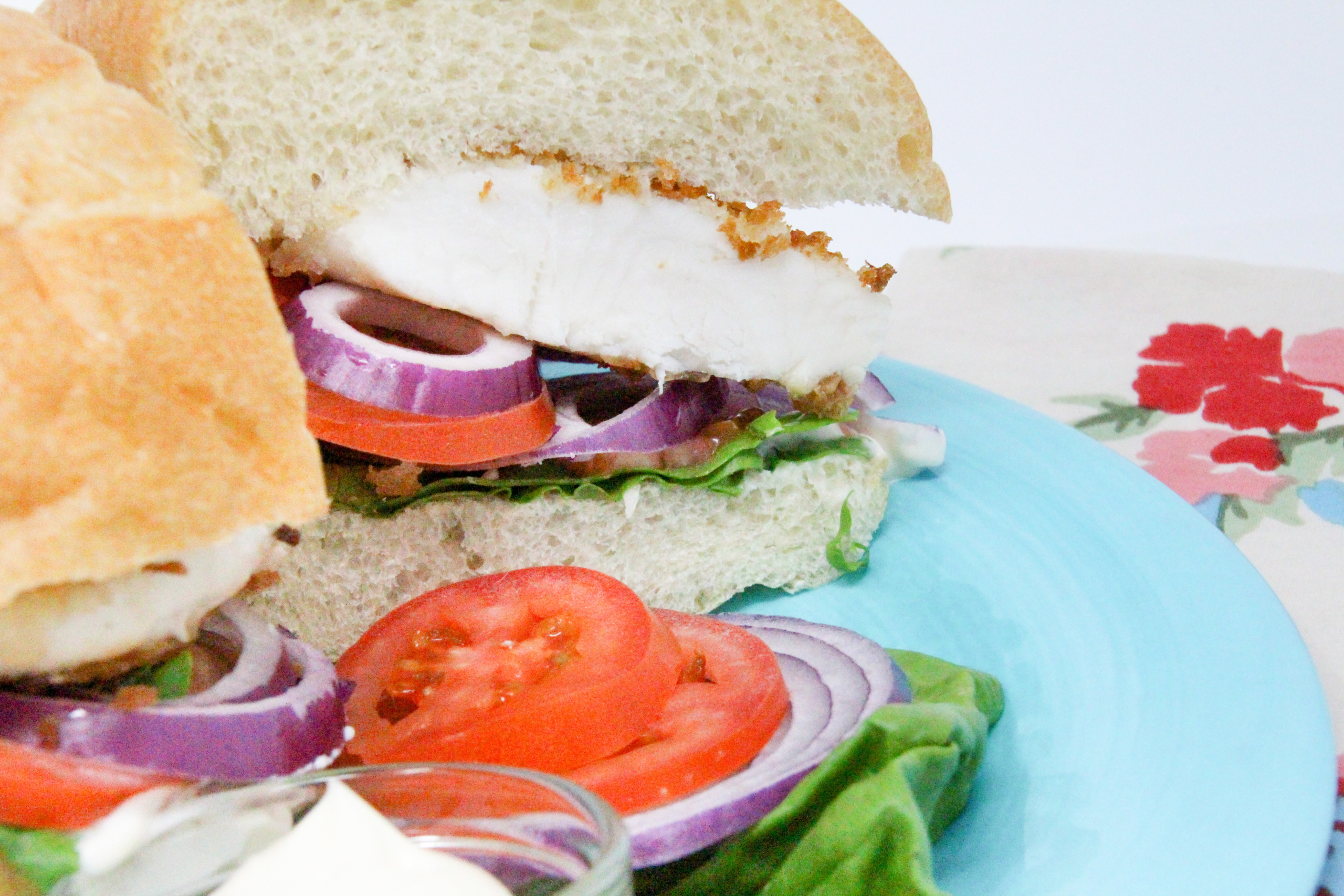 Fischbrötchen (German Fish Sandwich) uses a thin, pan-fried fillet, coated with breadcrumbs for a crispy exterior, and is layered with lettuce, red onions, peppers, and tomatoes for a delicious and hearty sandwich. Recipe shared with permission granted by T.C. LoTempio, author of MURDER FAUX PAWS.