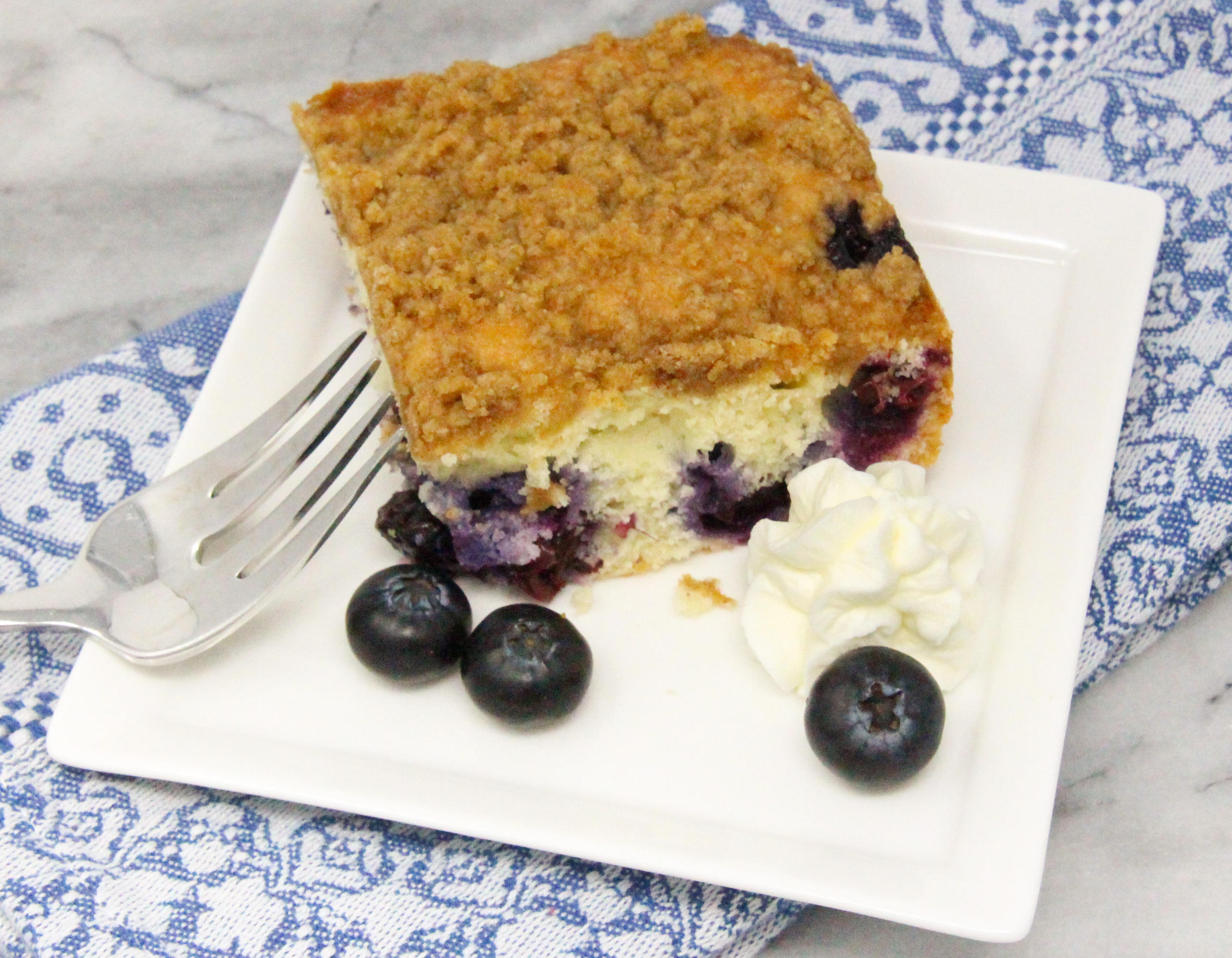 Blueberry Coffee Cake with Crumble is chock full of fresh blueberries in a tender vanilla cake. The cinnamon, brown sugar-based crumble adds both flavor and a pleasing crunchy texture. Recipe shared with permission granted by Krista Davis, author of A COLORFUL SCHEME. 