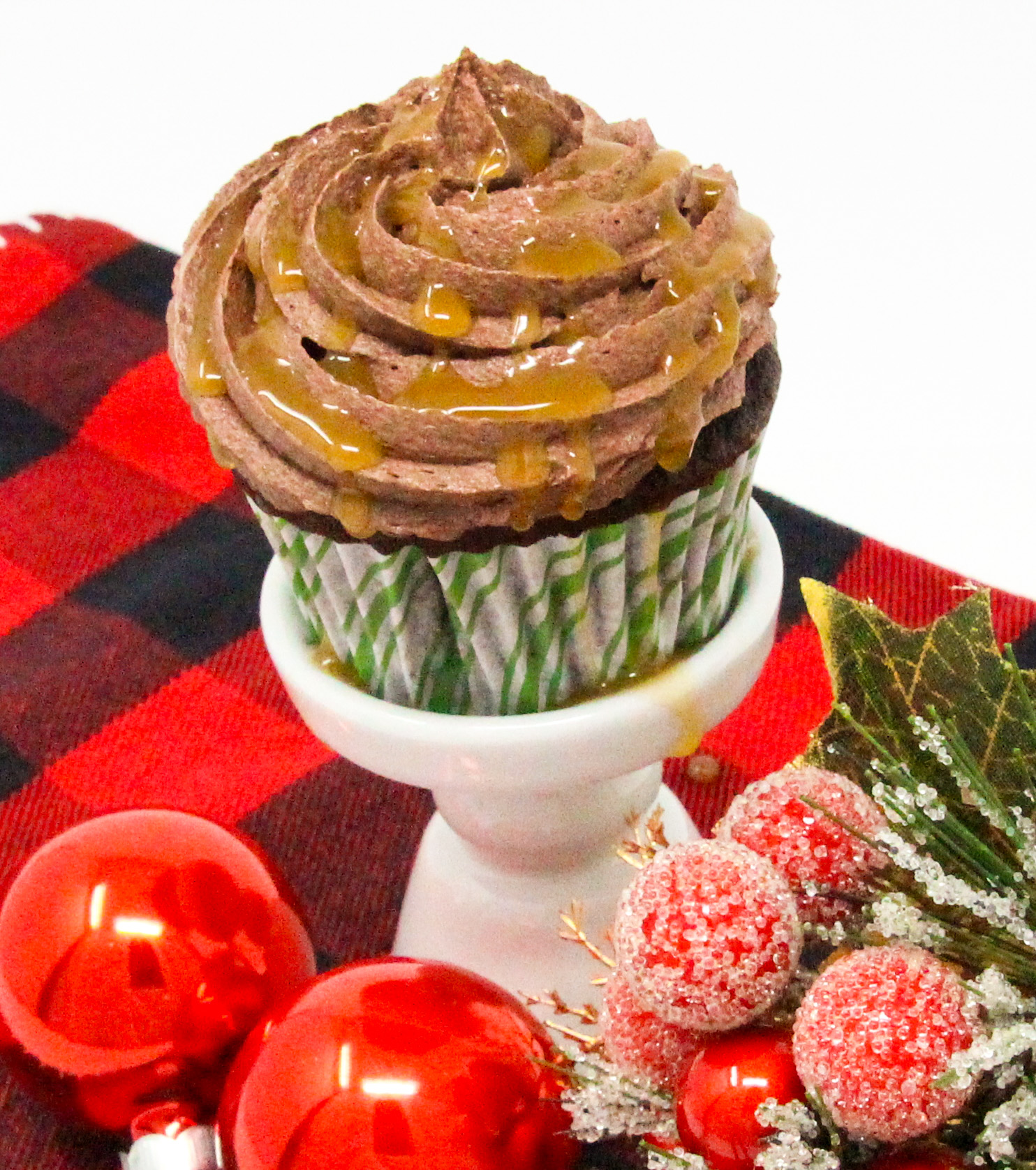 Christmas Caramel Cupcakes are rich, dark chocolate cupcakes, stuffed with homemade caramel, then topped with fudgy buttercream frosting and more caramel! Recipe shared with permission granted by Christina Romeril, author of A CHRISTMAS CANDY KILLING.