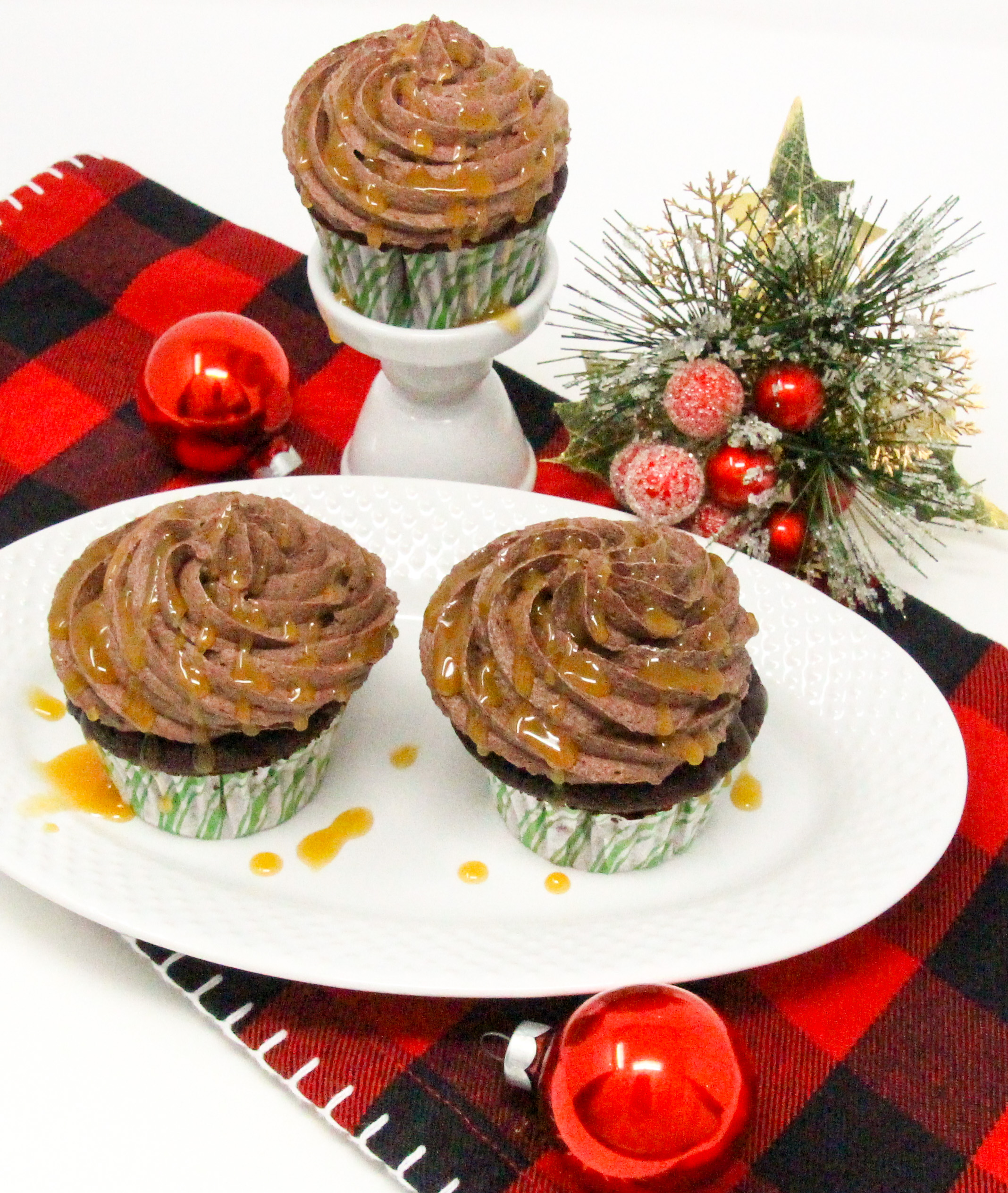Christmas Caramel Cupcakes are rich, dark chocolate cupcakes, stuffed with homemade caramel, then topped with fudgy buttercream frosting and more caramel! Recipe shared with permission granted by Christina Romeril, author of A CHRISTMAS CANDY KILLING.