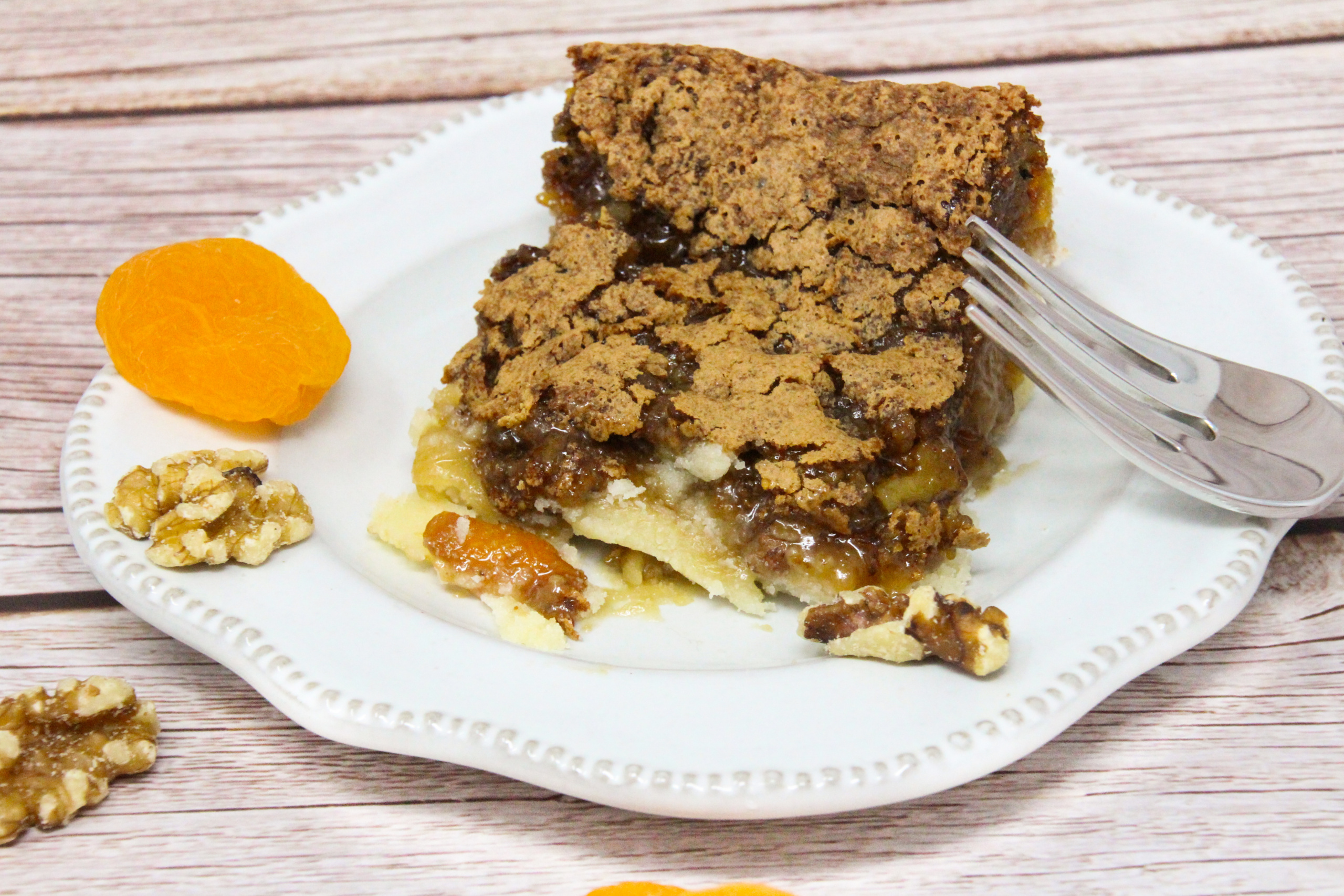 Apricot Squares start with a buttery base crust, and the filling is ooey-gooey and rich thanks to a generous portion of brown sugar, walnuts, and apricots. Recipe shared with permission granted by Barbara Ross, author of HIDDEN BENEATH. 