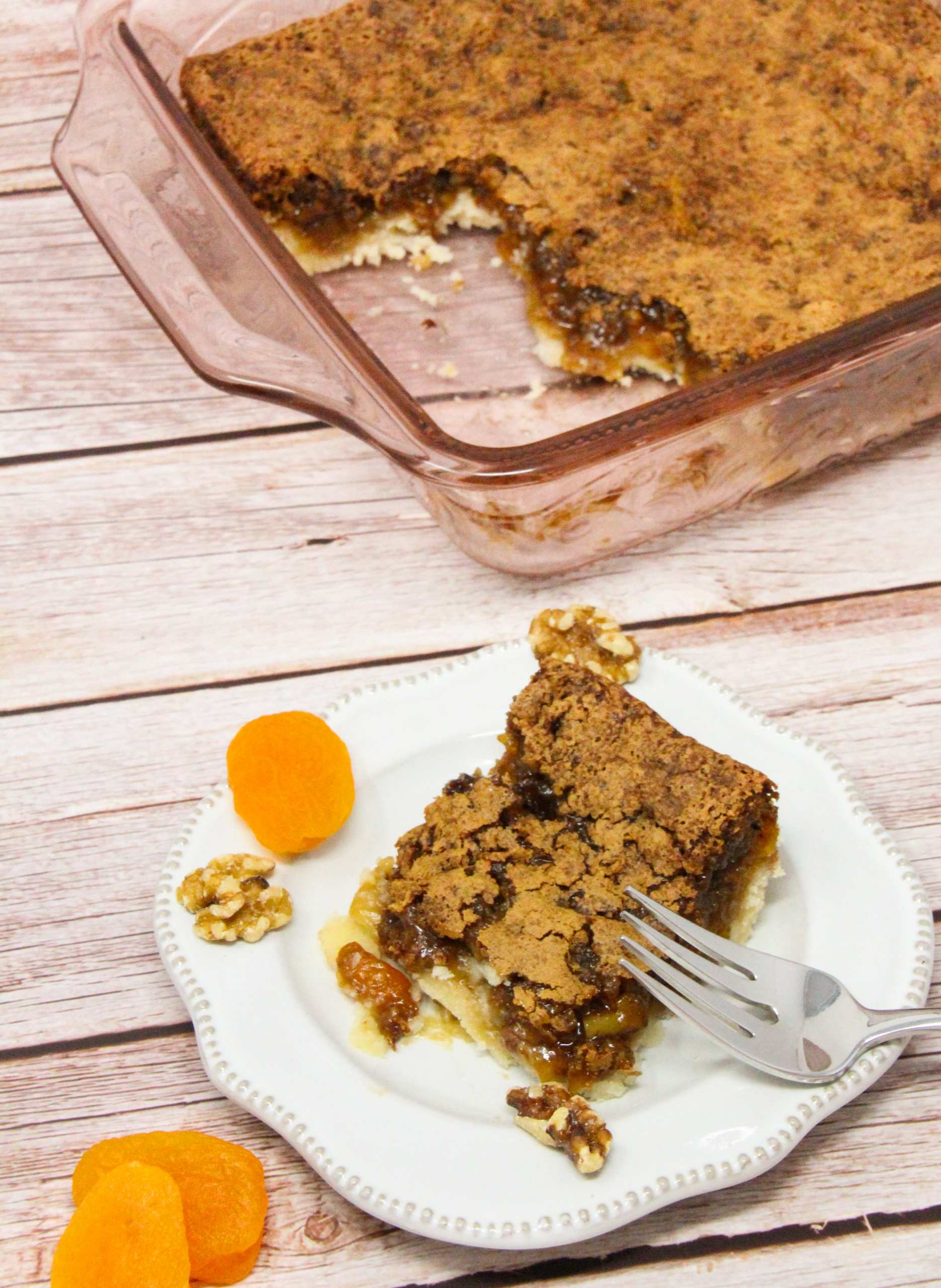 Apricot Squares start with a buttery base crust, and the filling is ooey-gooey and rich thanks to a generous portion of brown sugar, walnuts, and apricots. Recipe shared with permission granted by Barbara Ross, author of HIDDEN BENEATH. 