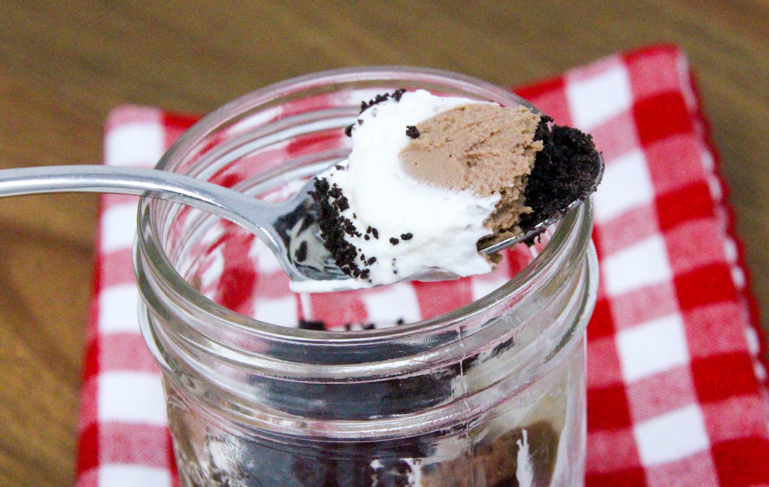 No-Bake Chocolate Cheesecake Jars are super easy-peasy to make with an Oreo crumb base. The delectable combination of chocolate, cream cheese, cream, sugar, and vanilla creates a silky layer of chocolate cheesecake, topped by cream cheese whipped cream. Layered in small mason jars, the presentation is fun and practical for easy serving for gatherings. Recipe shared with permission granted by Korina Moss, author of BAIT AND SWISS.