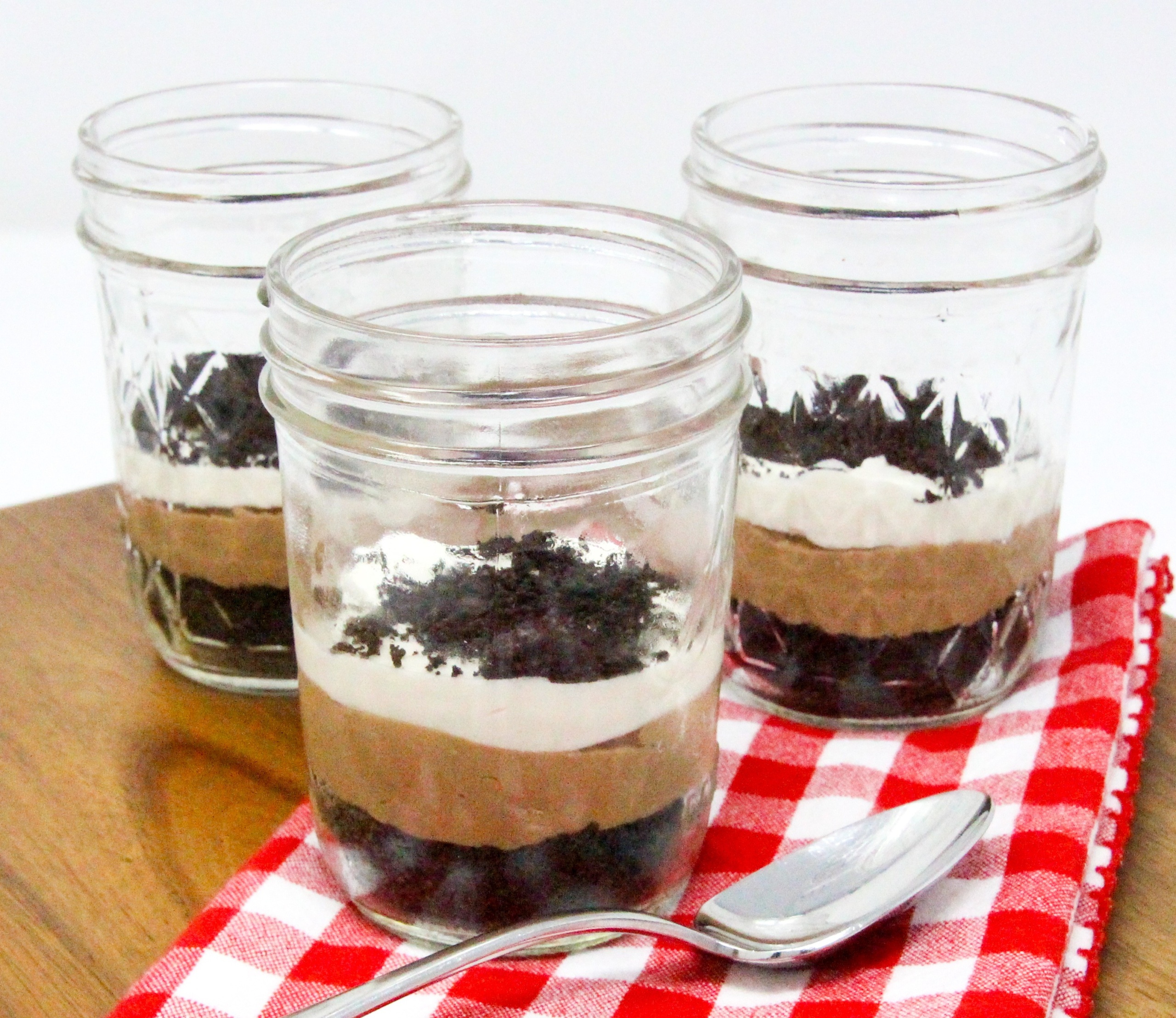 No-Bake Chocolate Cheesecake Jars are super easy-peasy to make with an Oreo crumb base. The delectable combination of chocolate, cream cheese, cream, sugar, and vanilla creates a silky layer of chocolate cheesecake, topped by cream cheese whipped cream. Layered in small mason jars, the presentation is fun and practical for easy serving for gatherings. Recipe shared with permission granted by Korina Moss, author of BAIT AND SWISS.