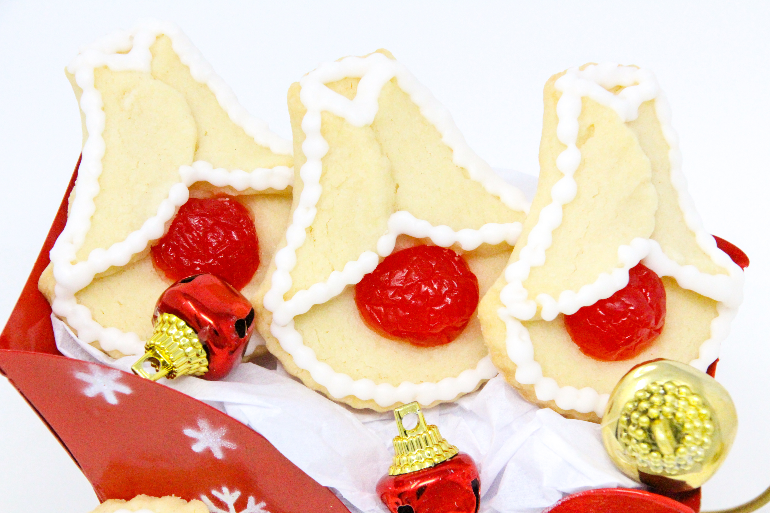 Cherry Bell Christmas Cookies start with a simple almond-flavored sugar cookie base, and are accented with halved maraschino cherries. These cookies will bring a touch of nostalgia to any holiday cookie platter and don't forget a plateful for Santa and his elves as well! Recipe created by Cinnamon & Sugar for SLEIGH BELLS AT MOONGLOW by Deborah Garner.