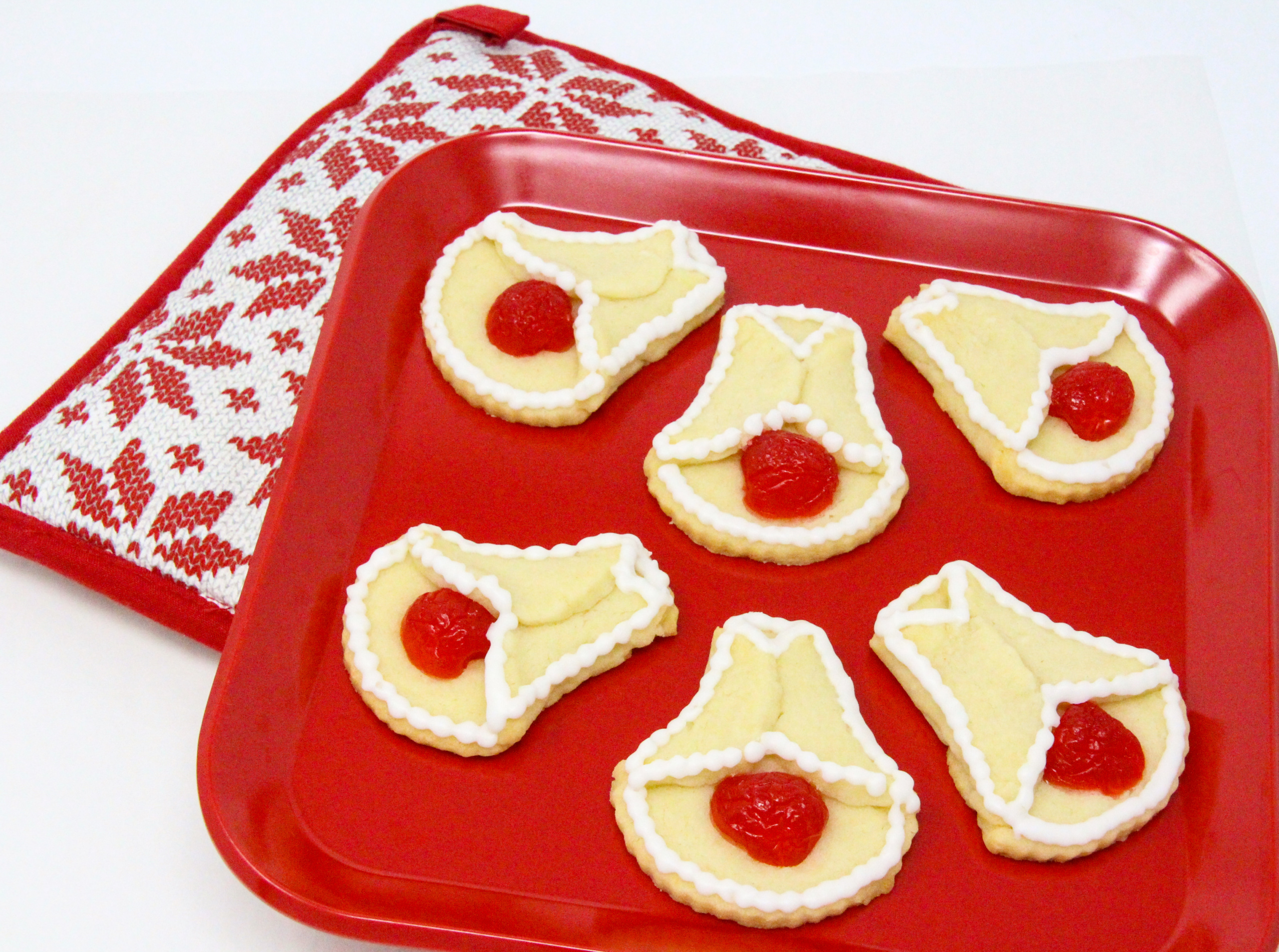 Cherry Bell Christmas Cookies start with a simple almond-flavored sugar cookie base, and are accented with halved maraschino cherries. These cookies will bring a touch of nostalgia to any holiday cookie platter and don't forget a plateful for Santa and his elves as well! Recipe created by Cinnamon & Sugar for SLEIGH BELLS AT MOONGLOW by Deborah Garner.
