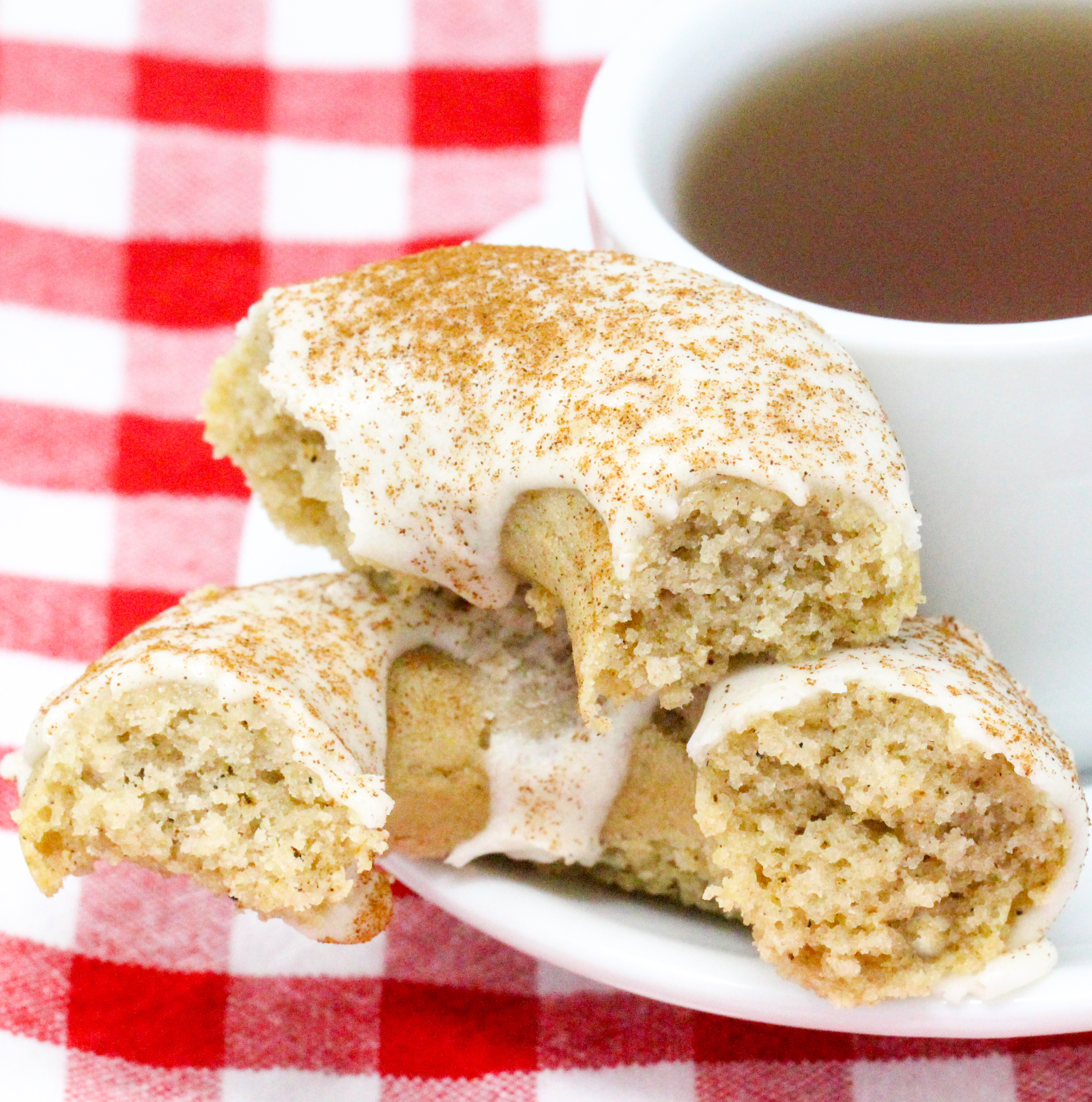 Spiced-Tea Baked Donuts have a rich flavor thanks to a generous amount of warming spices, while the sour cream frosting and sprinkled cinnamon adds a delicious element. These are delicious for breakfast or a coffee break snack! Recipe shared with permission granted by Ginger Bolton, author of SOUR CRIME DONUTS.