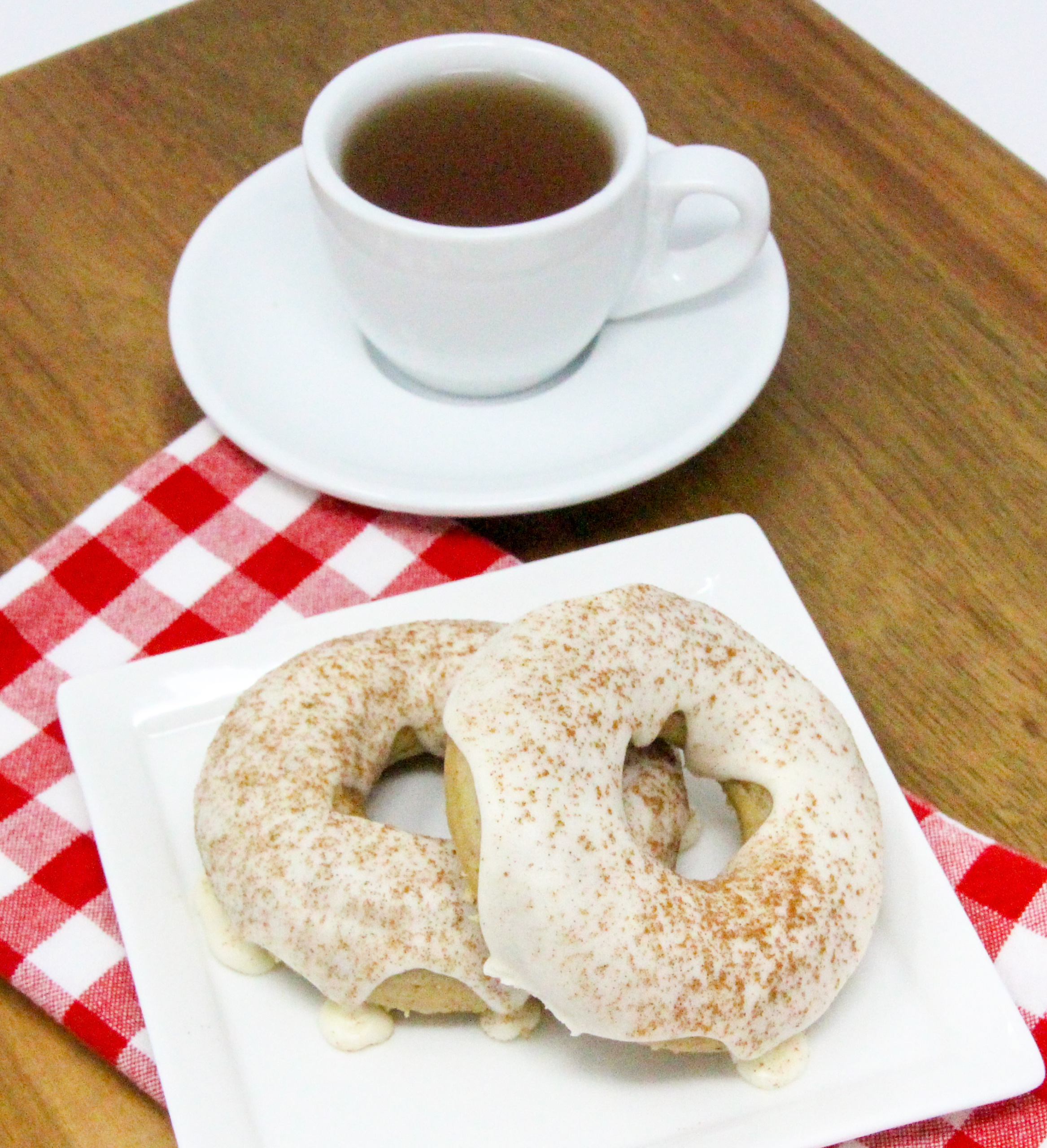 Spiced-Tea Baked Donuts have a rich flavor thanks to a generous amount of warming spices, while the sour cream frosting and sprinkled cinnamon adds a delicious element. These are delicious for breakfast or a coffee break snack! Recipe shared with permission granted by Ginger Bolton, author of SOUR CRIME DONUTS.
